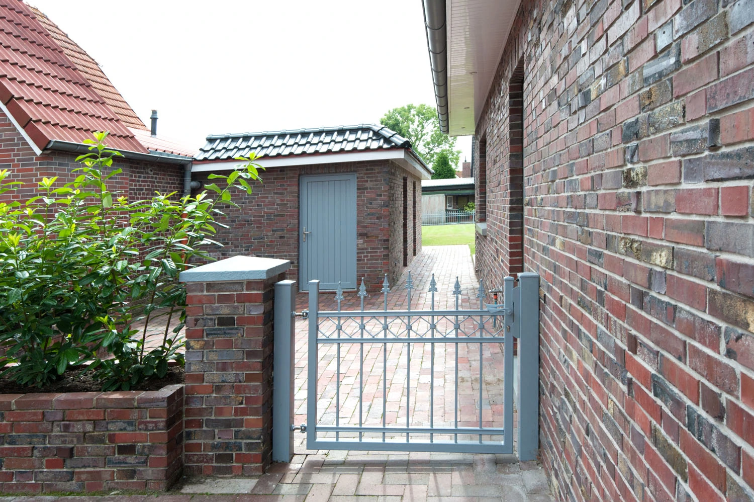 Gepflasterter Weg mit Metalltor und Backsteinmauer – Kunstreich Bauunternehmung Wittmund